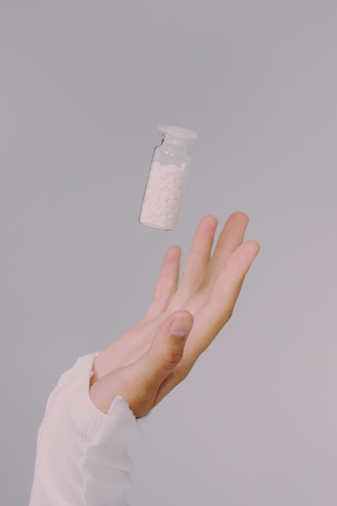En hånd under et lite glass med homeopatiske kuler